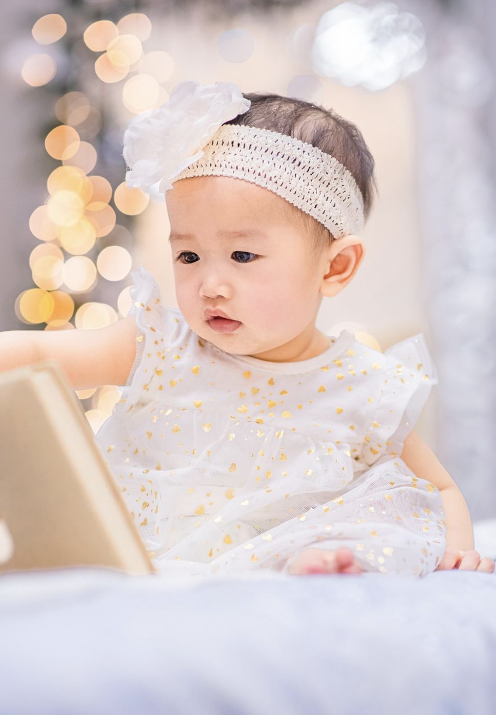 Baby girl in a white dress looking at a book