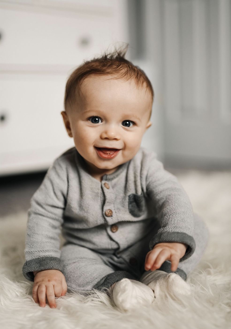 Baby in a grey romper sitting on a sheepskin rug