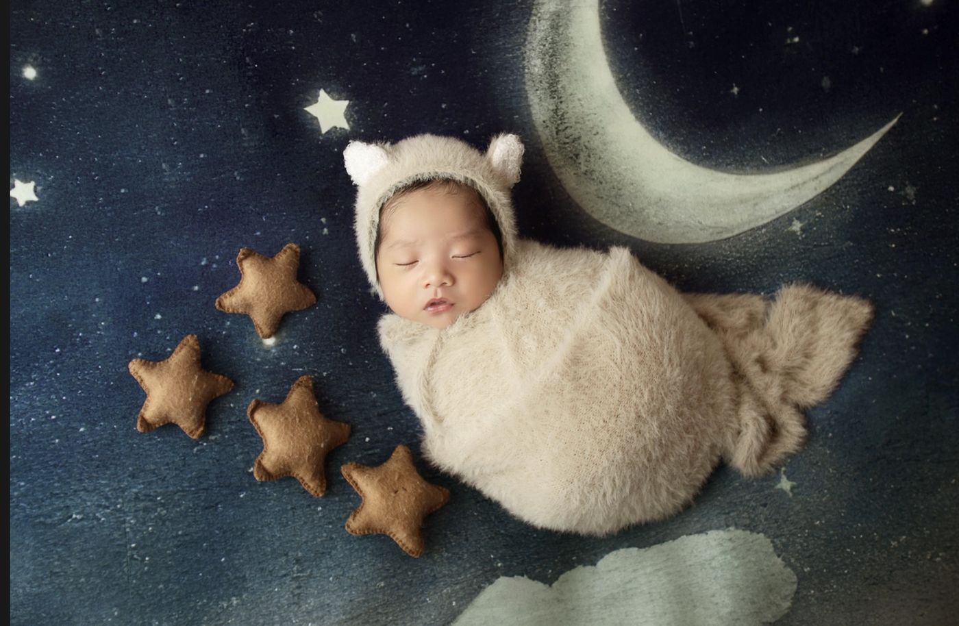 Swaddled newborn asleep against a starry night backdrop with a painted moon